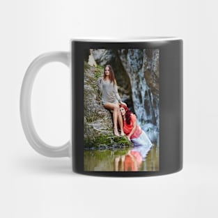 Two beautiful young women leaning on rocks beside a river Mug